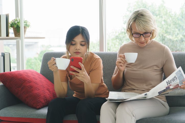 Mother and daughter sitting and reading on the smartphone and newspaper